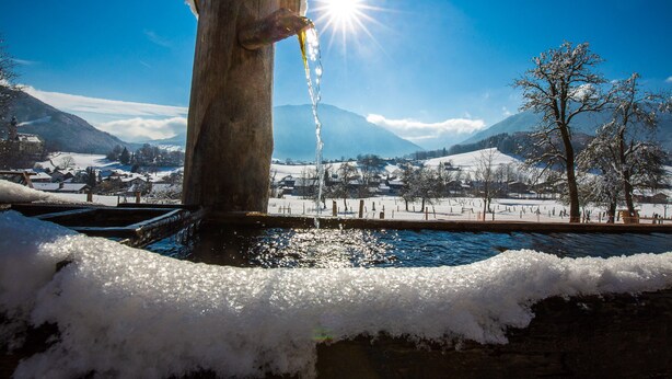 A wooden structure with water flowing from a spout, surrounded by snow and a clear sky. - Apartment Alm Stüberl, 65 square meters, balcony, 2 sep. Bedroom, max. 4 pers. (Ruhpolding)