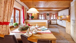 A cozy dining area with a wooden table set for two, a bench, and a kitchen in the background. - Apartment Alm Stüberl, 65 square meters, balcony, 2 sep. Bedroom, max. 4 pers. (Ruhpolding)