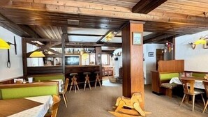 Een restaurant met houten balken in het plafond, groene bankjes en houten tafels en stoelen.