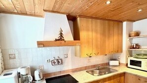 Een keuken met houten kastjes, een fornuis, een spoelbak en een magnetron.