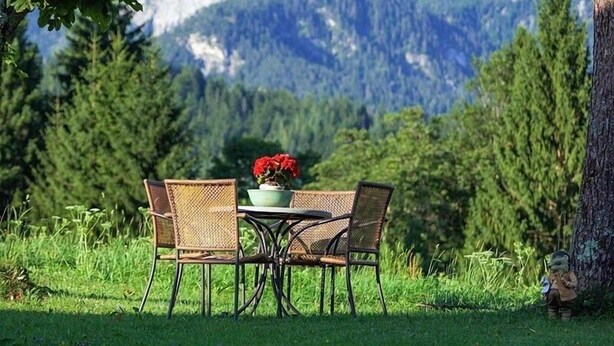 Een tafel met stoelen buiten, een bloempot en uitzicht op een bergketen.