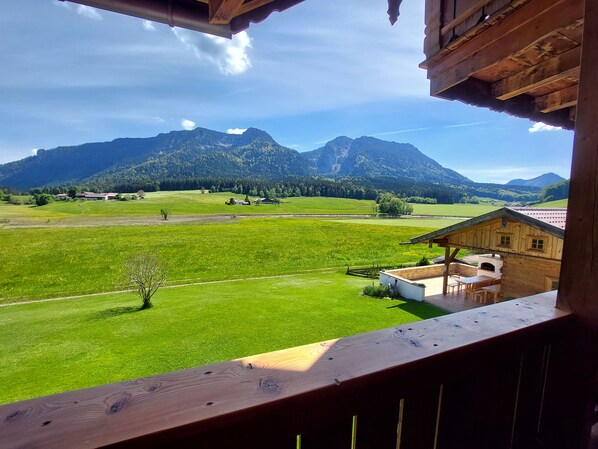 A wooden cabin with a balcony overlooking a green field and mountains.