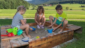 Three children playing with sand in a wooden sandbox outdoors. - Apartment Kienberg 38 sqm, balcony, kitchen, 1 bedroom, 1 bed-sitting room (Ruhpolding)