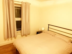 Una camera da letto con un letto, un comodino, una finestra con tende e uno specchio fissato al muro.