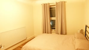 Una camera da letto con un letto, una finestra con tende, un termosifone e un comodino con una lampada.
