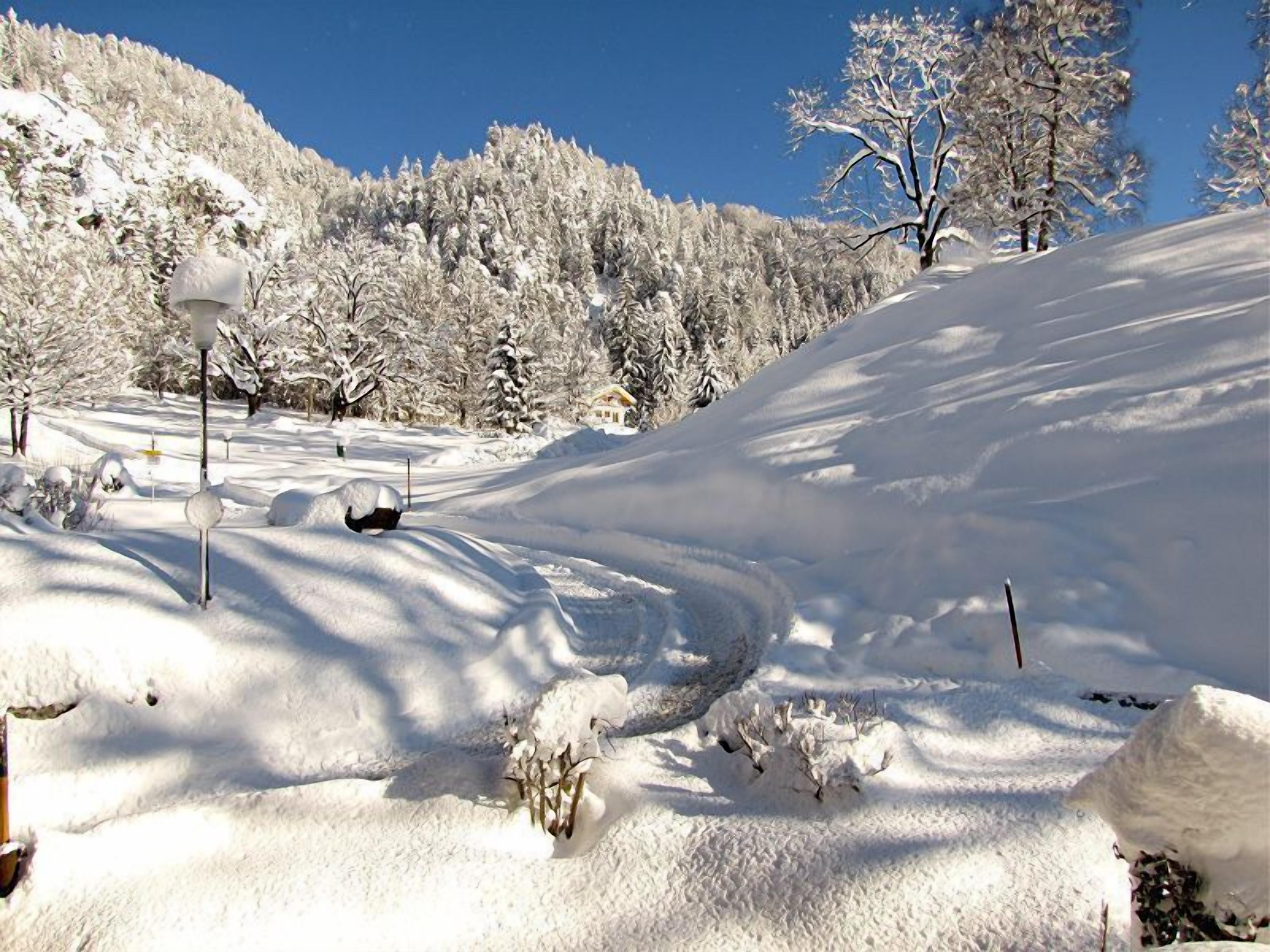 Schneebedeckte Landschaft mit blauem Himmel, einer Straße und vereinzelten Bäumen.
