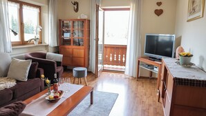 A living room with a sofa, coffee table, TV, wooden cabinet, and a view of the outdoors.