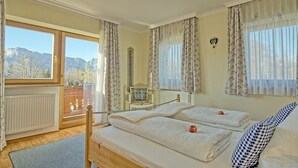 A bedroom with a bed, a window with curtains, a radiator, and a view of mountains.