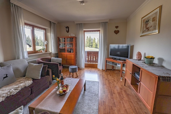 A living room with a sofa, a dining table with fruit, a television, and a cabinet.