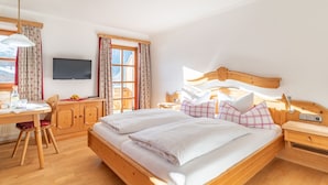 Hotellihuone, jossa on suuri sänky, puinen pääty, työpöytä tuolilla, televisio ja ikkuna, jossa on verhot.
