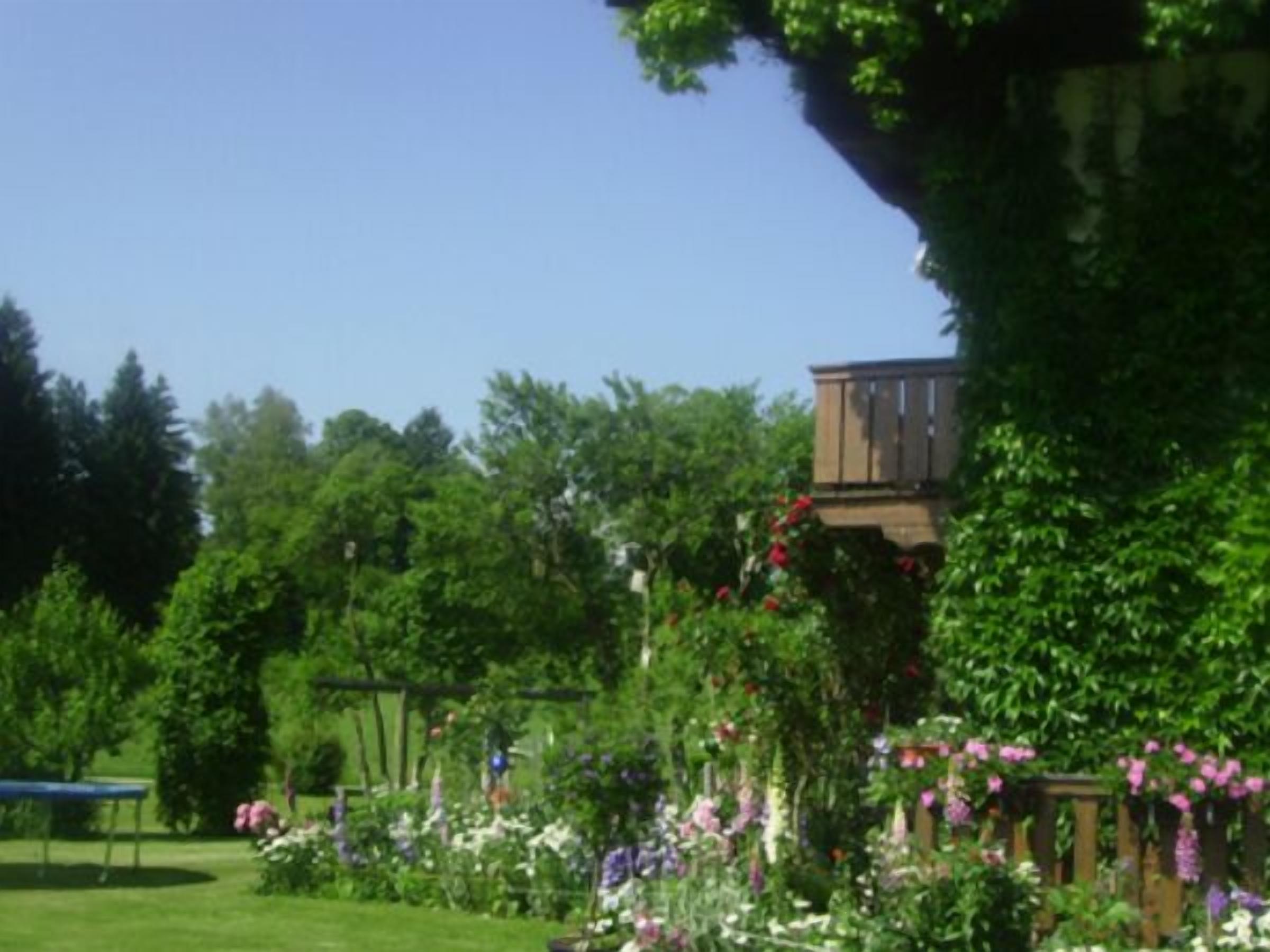 Ein Garten mit einer Holzterrasse, einer Bank und verschiedenen blühenden Pflanzen.