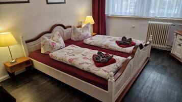 Ein Doppelbett mit floralem Bettzeug und Handtüchern, ein Nachttisch mit Lampe, ein Heizkörper und ein Fenster mit Vorhängen.