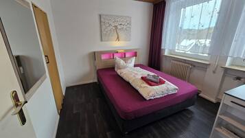 Een slaapkamer met een bed, een raam met gordijnen, een radiator en een houten plafond.