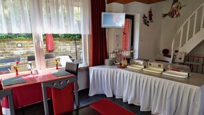Un área de desayuno con una mesa dispuesta para dos personas, un televisor montado en la pared y una escalera que conduce a un nivel superior.