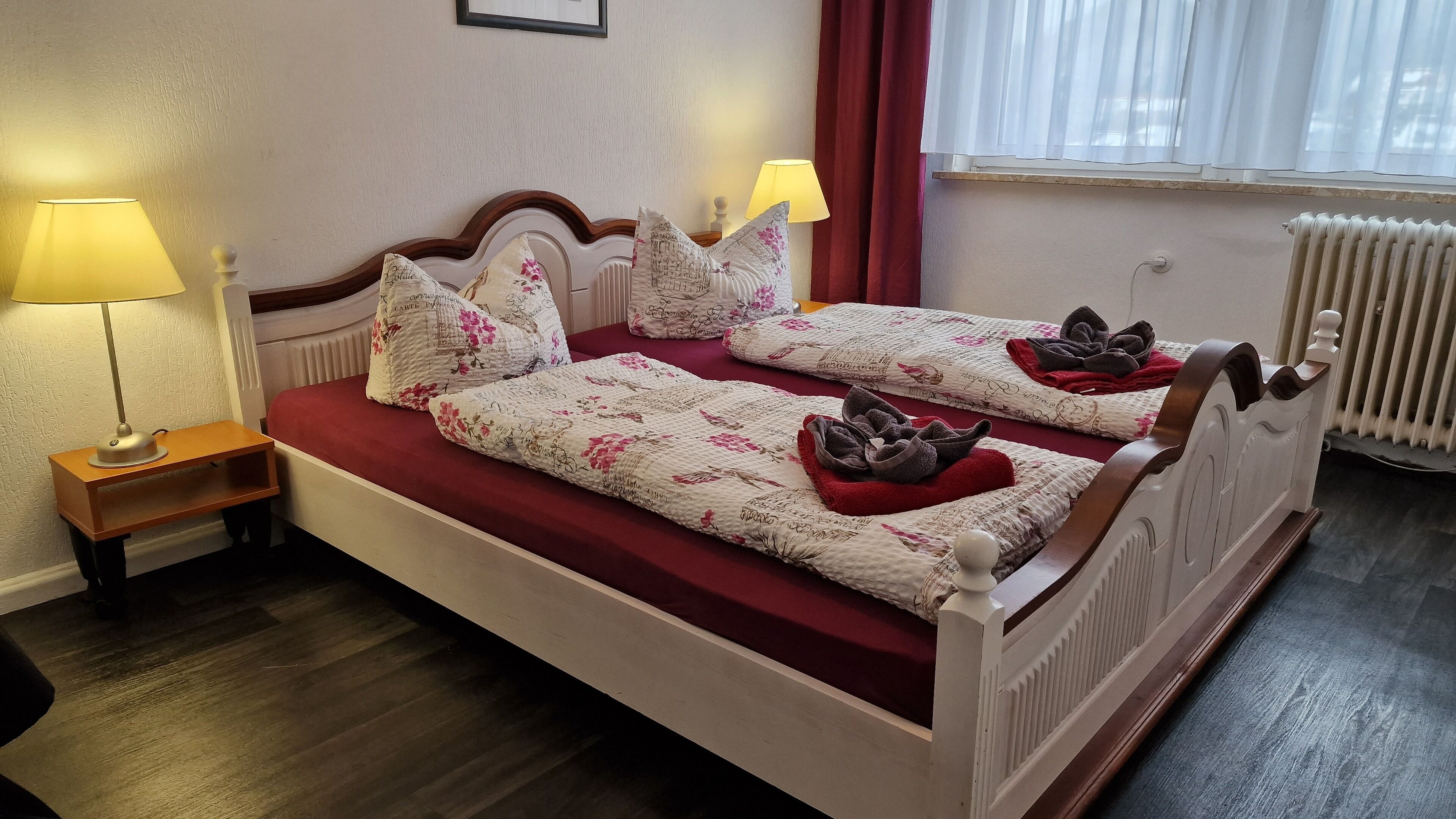 A double bed with floral bedding, two bedside lamps, and a radiator.