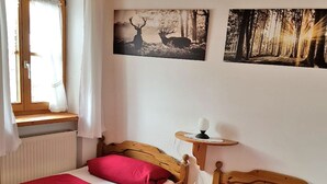 A bedroom with two beds, a window with curtains, a radiator, and two wall-mounted pictures of forests. - Ferienwohnung° II 45 qm, extra Schlafzimmer und Ost-Balkon° (Aschau im Chiemgau)