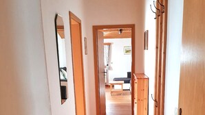 A hallway with wooden flooring and doors leading to a living area with a sofa and a table. - Ferienwohnung° II 45 qm, extra Schlafzimmer und Ost-Balkon° (Aschau im Chiemgau)