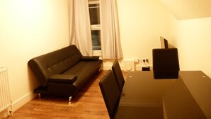 Ein Zimmer mit einer schwarzen Couch, einem kleinen Tisch und einem Fernseher auf einem Schrank.