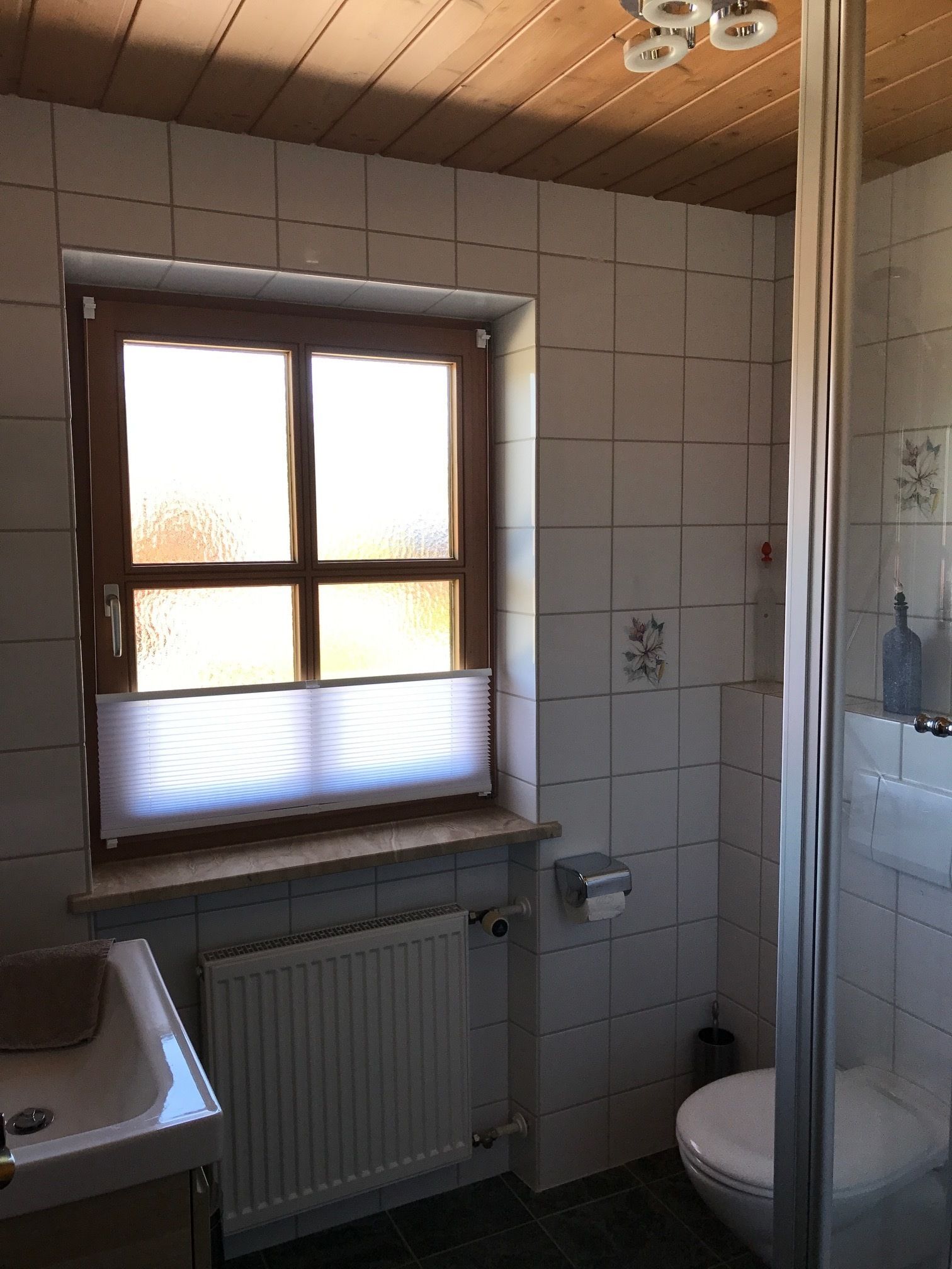 A bathroom with a window, a radiator, a toilet, and a shower area.