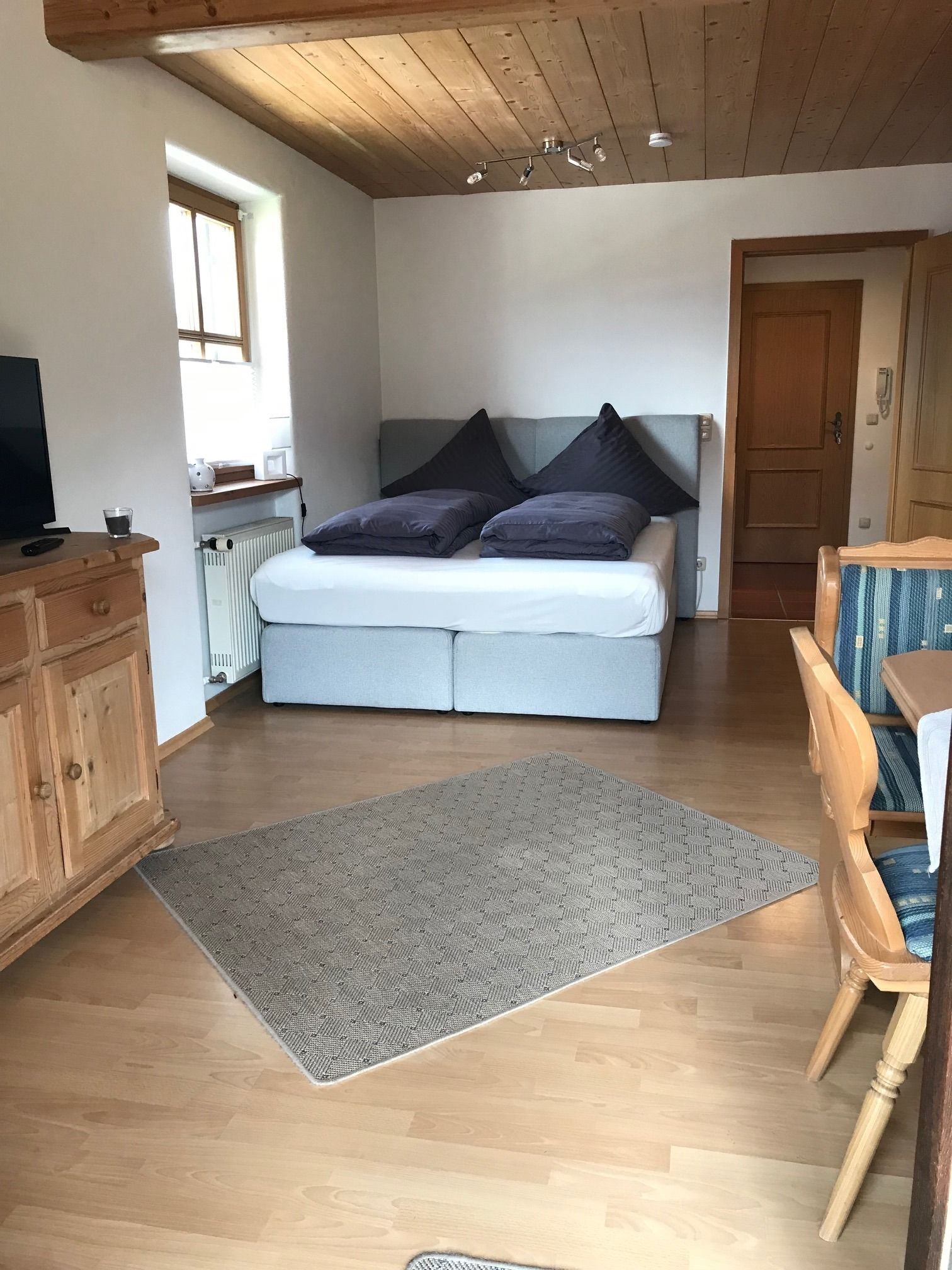 Une chambre à coucher avec un lit, une commode en bois, un téléviseur et une fenêtre.