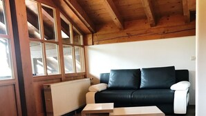 A cozy living room with a wooden ceiling, a black leather sofa, and a white coffee table. - Haus am Dürrach (Reit im Winkl)