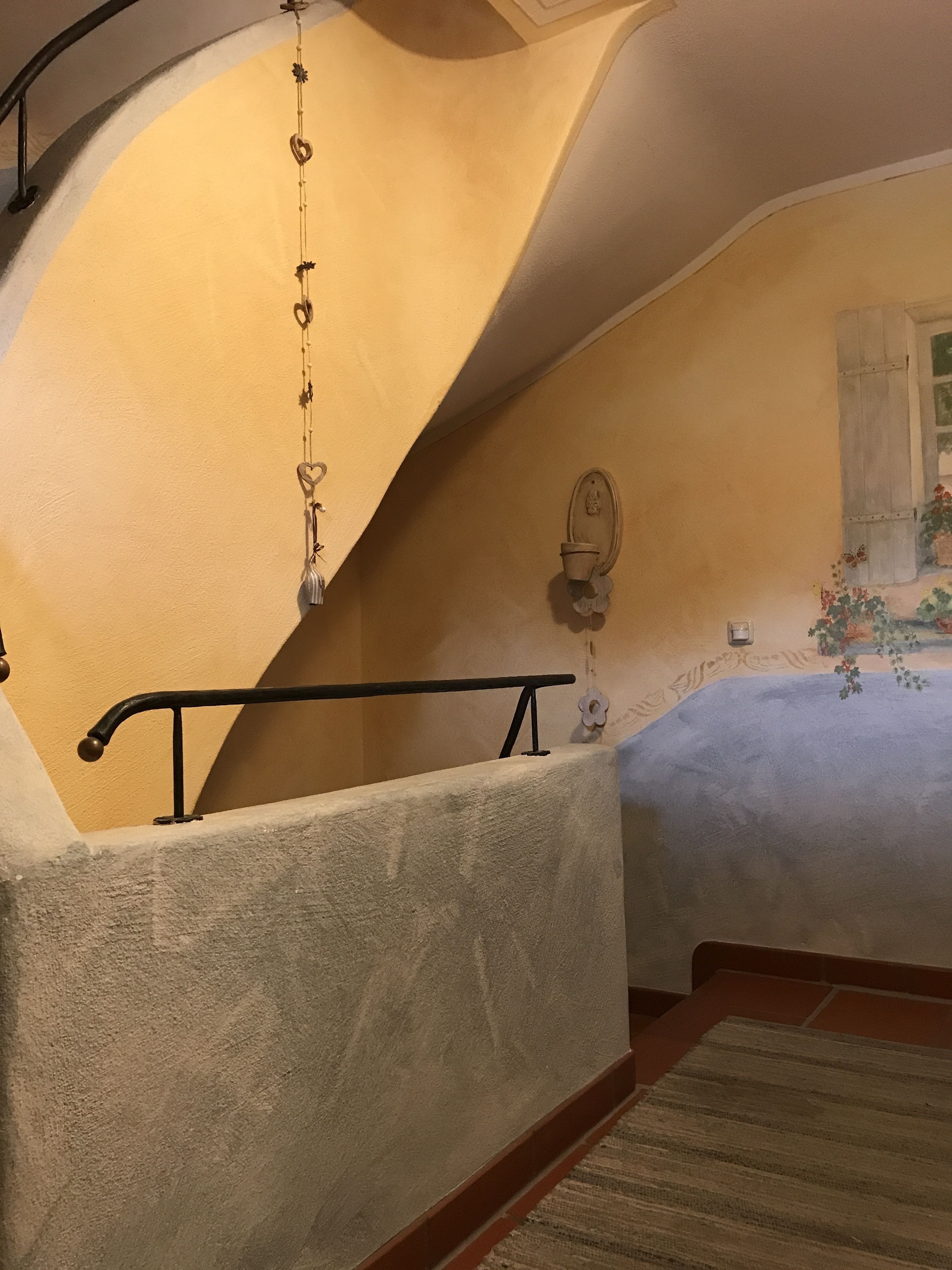 Un dormitorio con techo curvo, una cama con cubrecama floral, una mesita de noche y una lámpara de pared.