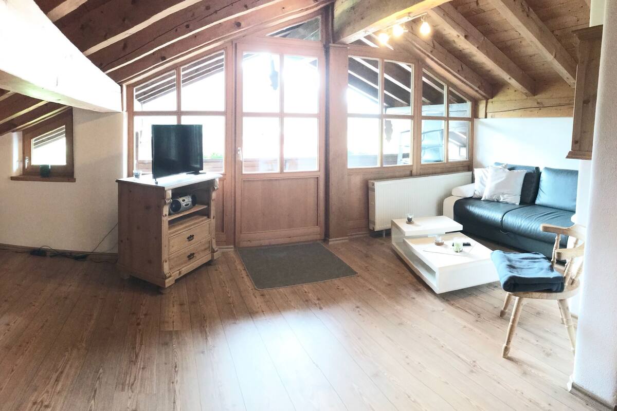 A cozy attic room with a wooden ceiling, a sofa, a TV, and a window with a view.