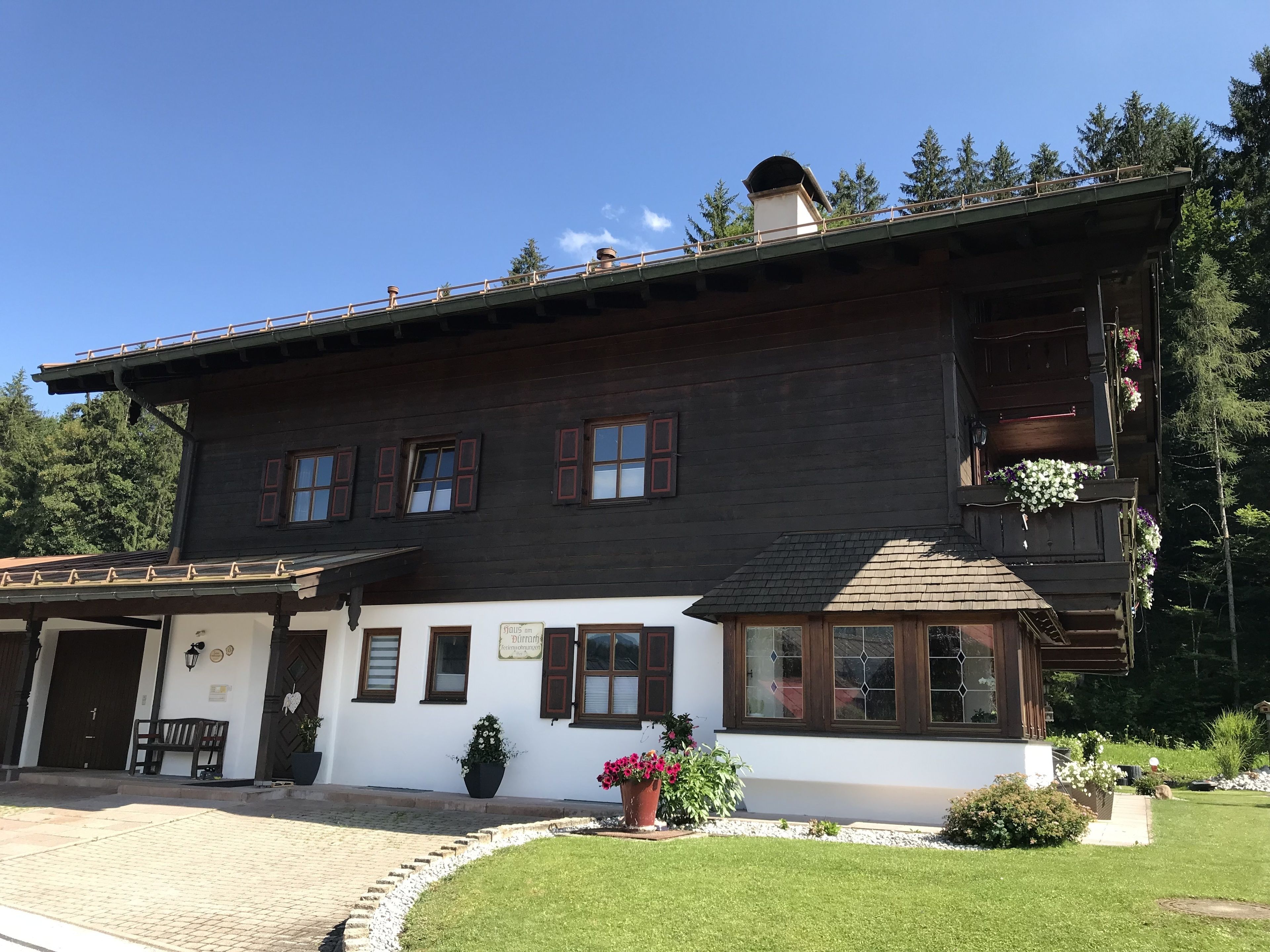 A two-story wooden house with a balcony, a front porch, and a small garden area.