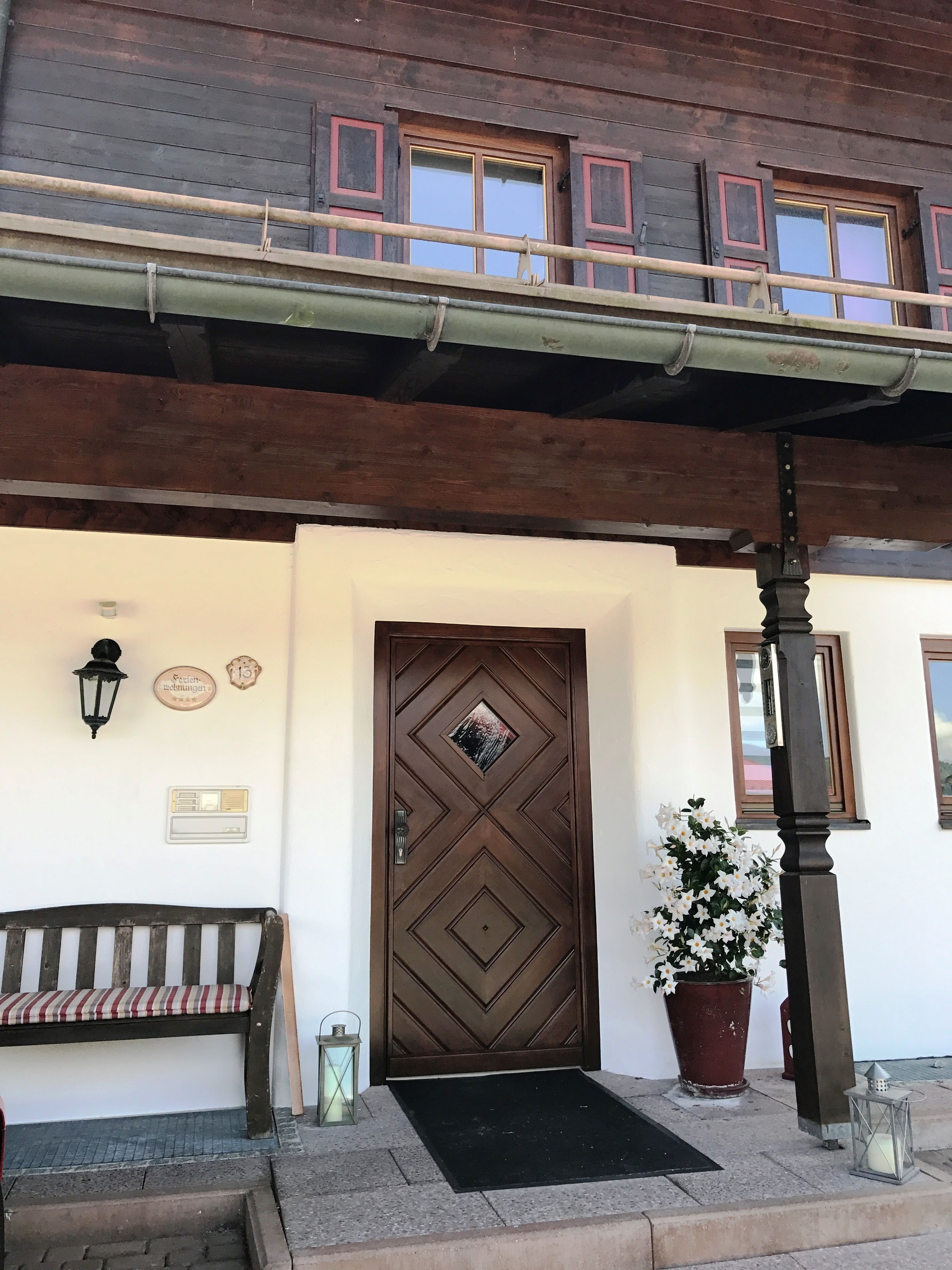 A wooden building with a large, ornate door, a bench, and a potted plant.