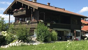 A wooden chalet with a balcony, surrounded by greenery and a stone wall. - Haus am Dürrach (Reit im Winkl)