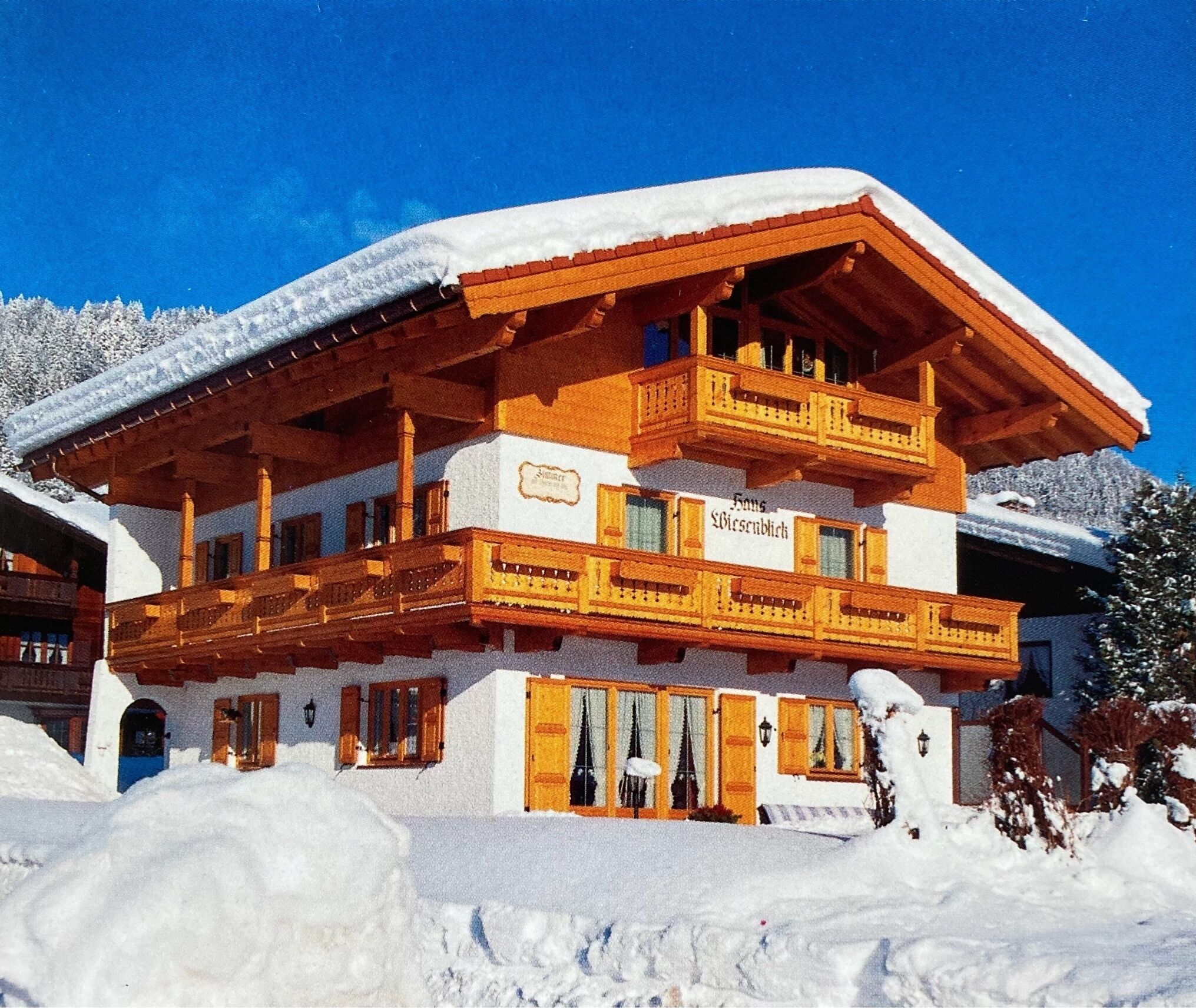 Een chalet van hout met twee verdiepingen en een balkon, omgeven door sneeuw.