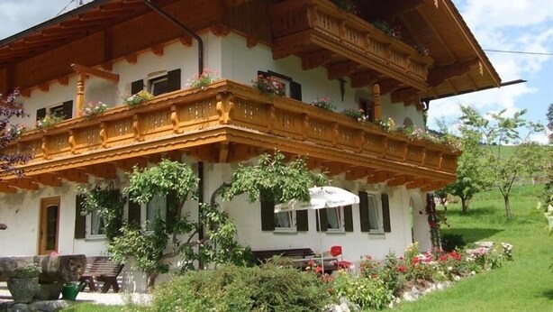 Un tipico chalet con un balcone in legno, un giardino fiorito e un cielo sereno.