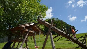 Una struttura di gioco in legno rustica con uno scivolo e altalene in un prato erboso.