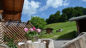 Una baita di legno con un recinto di legno a griglia, un tavolo di legno con un vaso di fiori e una collina erbosa sullo sfondo.