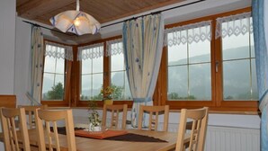 Zona pranzo con tavolo e sedie in legno, ampie finestre con tende e lampadario.