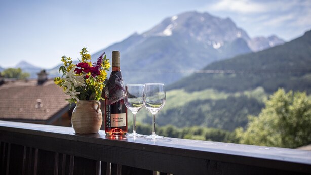 Una botella de vino y dos copas en un balcón con vista a la montaña.