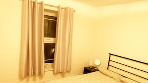 Un dormitorio con cama, mesita de noche con lámpara y ventana con cortinas.
