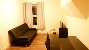 Una habitación pequeña y poco amoblada con un sofá, un televisor y un escritorio.