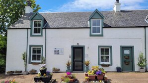 A white building with green trim, a black door, and multiple flower planters in front. - The House at Glenbarr (Tarbert)