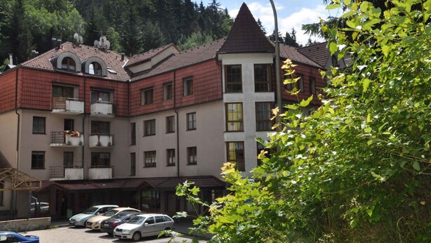 Un immeuble à plusieurs étages, doté d’une façade en briques rouges, de nombreux balcons et d’un parking où sont stationnées plusieurs voitures.