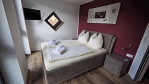Un dormitorio con cama, una mesita de noche, televisor montado en la pared y una ventana.
