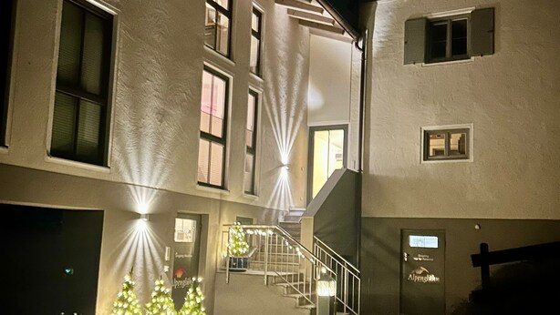 Un edificio con varias ventanas y una escalera que conduce a un piso superior. Hay árboles de Navidad en macetas con luces en primer plano.