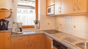 Une cuisine avec des meubles de rangement en bois, un four à micro-ondes, une machine à café et une fenêtre avec des rideaux.