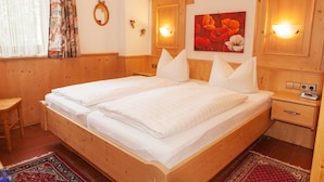 Un lit double avec du linge de lit blanc, une tête de lit en bois, des lampes de chevet et un tableau représentant des fleurs accroché au mur.