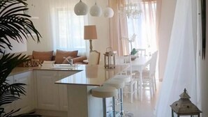 Una cocina moderna con una isla central, taburetes de bar, luces colgantes y un comedor con sillas y una mesa.
