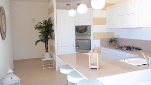 Una cocina moderna con gabinetes blancos, una isla central con taburetes, iluminación colgante y una estufa a gas.