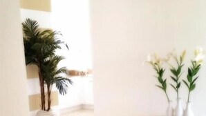 Un espacio amplio y luminoso con diseño moderno, que incluye un gran ventanal, una pequeña mesa blanca con una planta y un jarrón decorativo con flores.