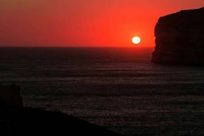 A sunset over a body of water with a cliff on the right. - Kantra Residence (Munxar)