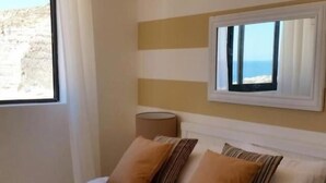 Una habitación de hotel con una cama, una ventana que ofrece vistas a la playa y un diseño de pared a rayas.