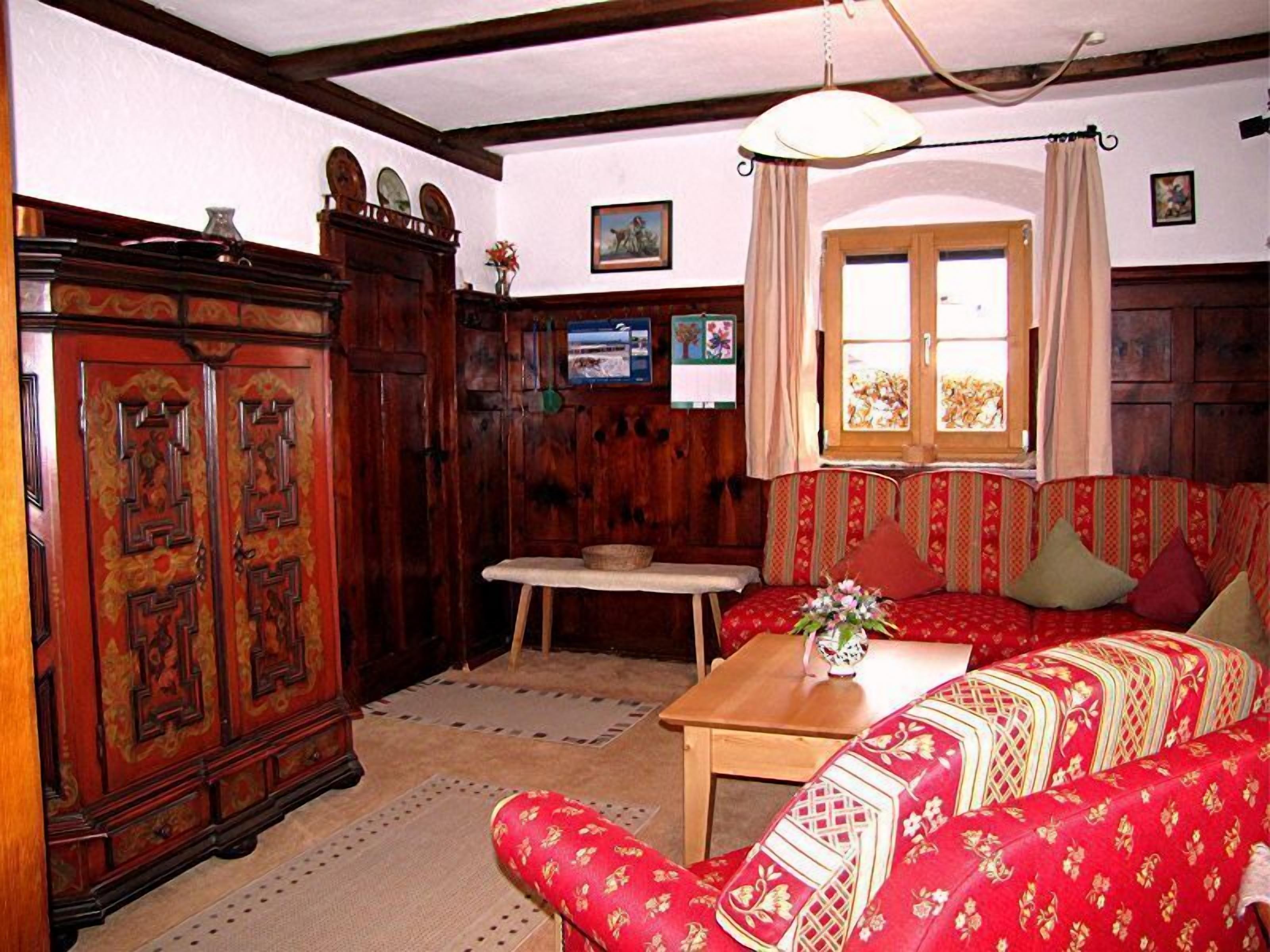 A traditional room with a wooden cabinet, a sofa, a table, and a window with curtains.